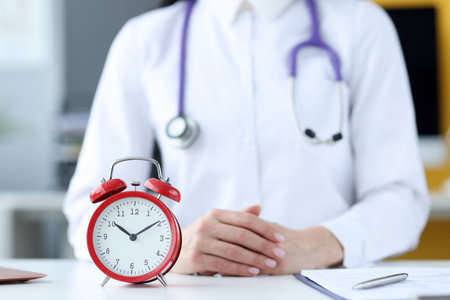 Doctor therapist sitting in office in front of red alarm clock closeup. Doctors schedule conceptの写真素材