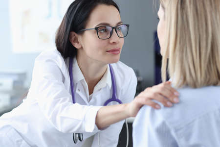 Female doctor looking at patient and holding her shoulder. Psychological support conceptの写真素材