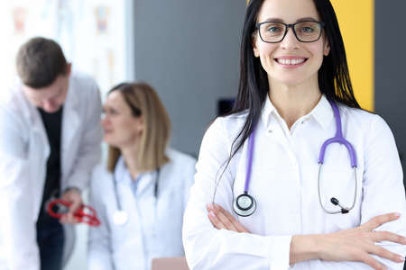 Portrait of smiling female doctor on background of colleagues. Medical professional assistance...