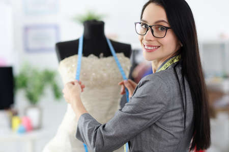 Female stylist stands next to mannequin wearing wedding dress. Salon for sewing and selling wedding...