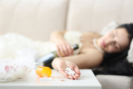 Bride in wedding dress lies on couch with pills in her hand. Bride suicide conceptの写真素材