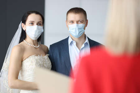 Man and woman in wedding suits and medical protective masks at ceremony. Weddings in coronavirus...