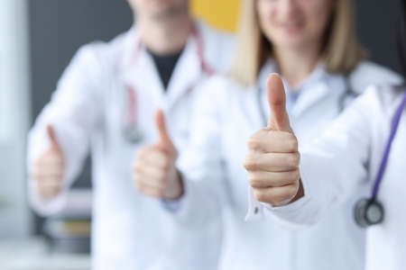 Three doctors stand behind each other and hold their thumbs up. Medical care and services of insurance companies conceptの写真素材