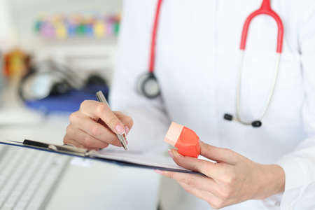 Pulmonologist holding inhaler in hands and writing in documents closeup. Bronchial asthma treatment conceptの写真素材