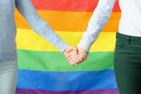 Two young women holding hands against lgbt flag background. Rights of sexual minorities conceptの写真素材