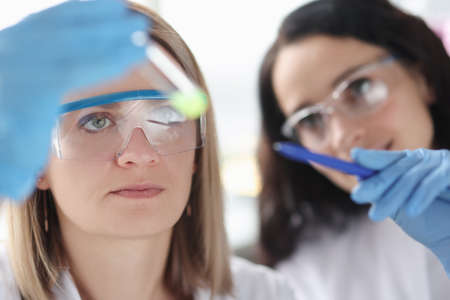 Two female scientists in laboratory examine test tube with liquid. Development of new chemical compounds conceptの写真素材
