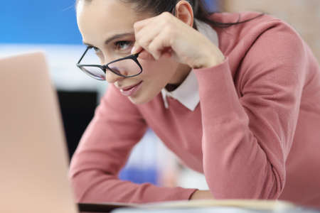 Portrait of woman who takes off her glasses and looks carefully at laptop screen. Concentrating on...