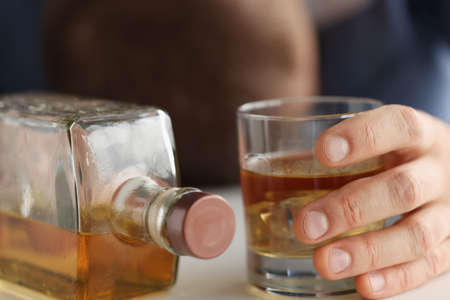 In mans hand glass with alcohol next to bottle. Alcohol addiction conceptの写真素材