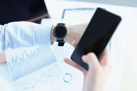Man holds smartphone in his hand and looks at smart watch. Smart watch for health monitoring conceptの写真素材