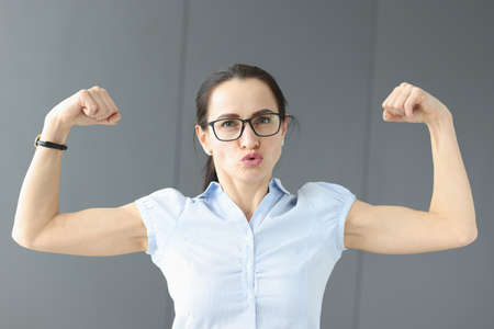 Young woman in glasses showing muscles on her arms. Bodycare concept