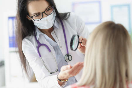 Doctor examining skin on patients face using magnifying glass. Skin examination conceptの写真素材