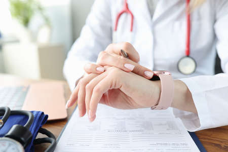 Doctor looks at clock at work table in medical office. Irregular working hours for health workers conceptの写真素材