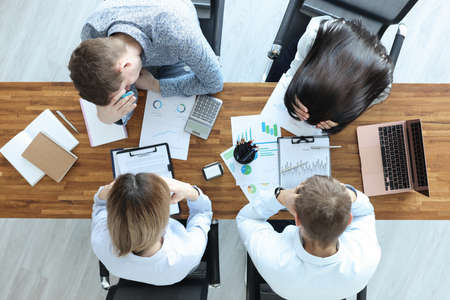 Group of people sitting at table and holding their heads top view. Solving business problems conceptの写真素材