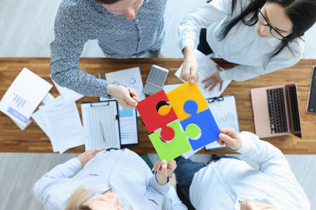 Group of business people are sitting at table and putting together colorful puzzle top view. Business strategy conceptの写真素材