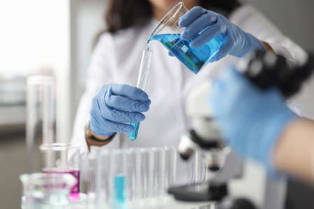 Lab technician with gloves pours chemical into test tube. Scientific research in chemical industry...