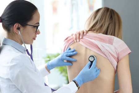 Doctor therapist listening to lungs of patient from back. Diagnosis of pneumonia concept