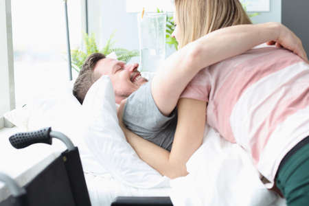 Joyful man hugs woman on hospital bed. Quick recovery from illness conceptの写真素材