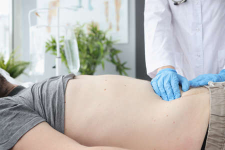 Doctor examines patient's abdomen on couch. Bowel disease and indigestion conceptの写真素材