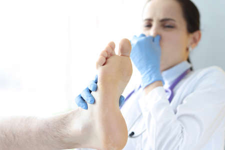 Doctor covers nose from unpleasant smell from male legの写真素材