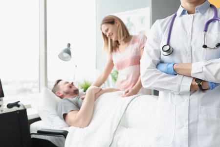 Happy man lies on hospital bed his hand is held by woman next to doctorの写真素材