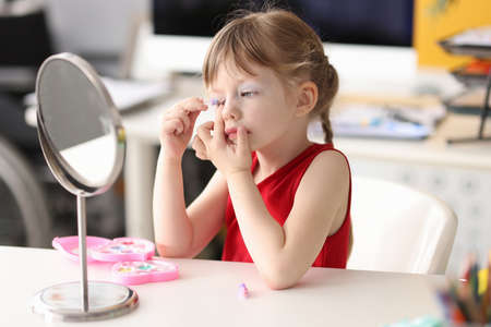 Little girl paints her eyes and looks in mirrorの写真素材
