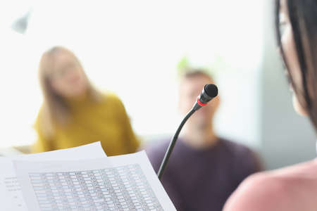 Woman in front of microphone reading information from paper closeupの写真素材