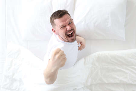 Young man lying in bed and rejoicing top viewの写真素材