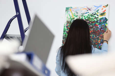 Brunette woman hangs her painted picture on wallの写真素材
