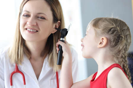 Little child examining doctor ear with otoscope in clinicの写真素材