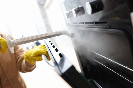 Woman in protective gloves washing oven with steam brush closeupの写真素材