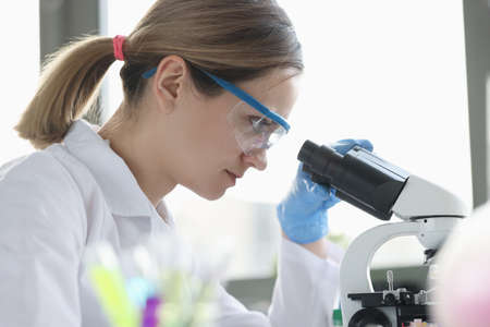 Woman scientist with glasses conducts research through microscopeの写真素材