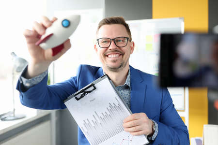 Smiling man holding rocket and business charts in his handの写真素材