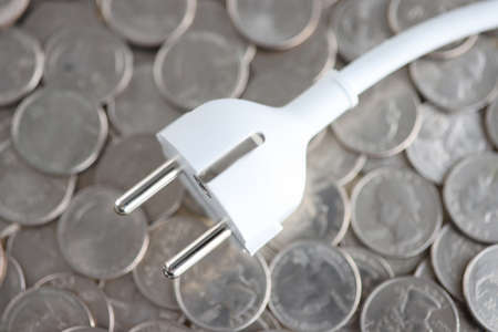 Electric plug lying on pile of coins closeupの写真素材