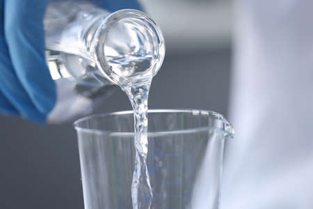Scientist chemist in gloves pouring water from flask into glass closeupの写真素材