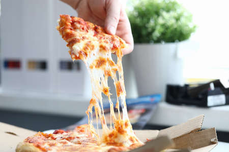 Hand takes a piece of delicious hot pizza closeup