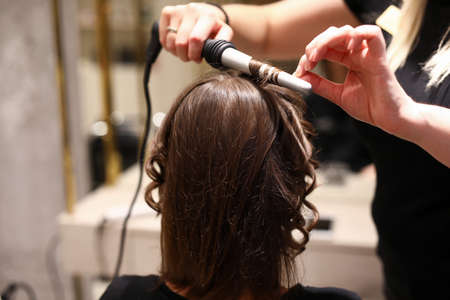 The hairdresser curls his hair with a curling ironの写真素材
