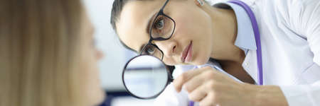 Doctor examines the patients face through magnifying glassの写真素材