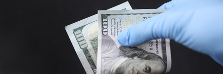 Gloved hand holds hundred dollar bill closeup
