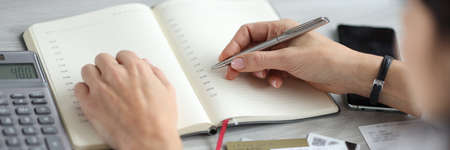 Female hand holds pen over diary near bank cards and calculator.の写真素材