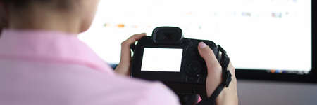 Woman sits at computer and holds camera.の写真素材