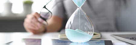 Female hand on desktop holds an hourglass.