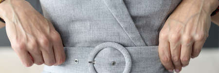 Woman straightening her belt on gray dress with her hands close-upの写真素材