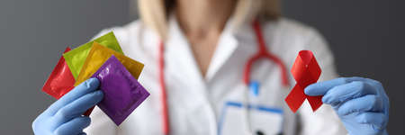 Doctor in protective gloves holding red ribbon and condoms closeupの写真素材