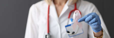 Doctor holding pink ribbon in his hand in rubber glove closeup