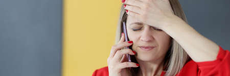 Woman is talking on phone and holding her forehead with her hand