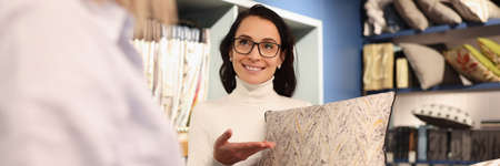 Woman holding pillow in her hands in workshop. Client selecting fabric from catalog