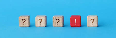 Red wooden cube with exclamation mark lying among cubes with question marks closeupの写真素材