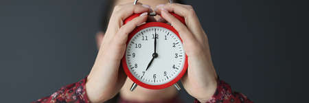 Female hands holding red alarm clock in front of face closeup