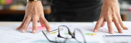 Business woman putting hands on table near glasses and documents with graphs closeup