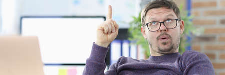 Pensive man sits at work table and holds thumbs up